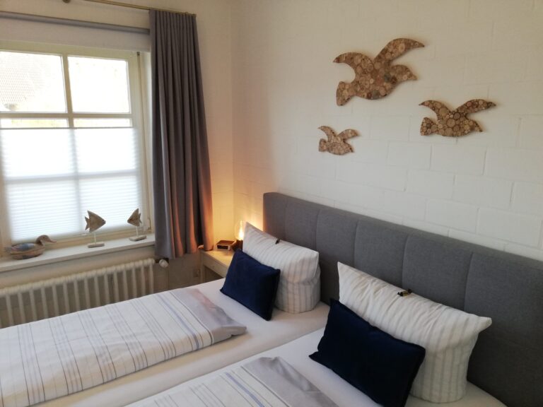 Bezogenes Doppelbett mit zwei Kissen und Bettdecken, an der Wand dekorative Möwen aus Holz und ein Blick aufs Fenster