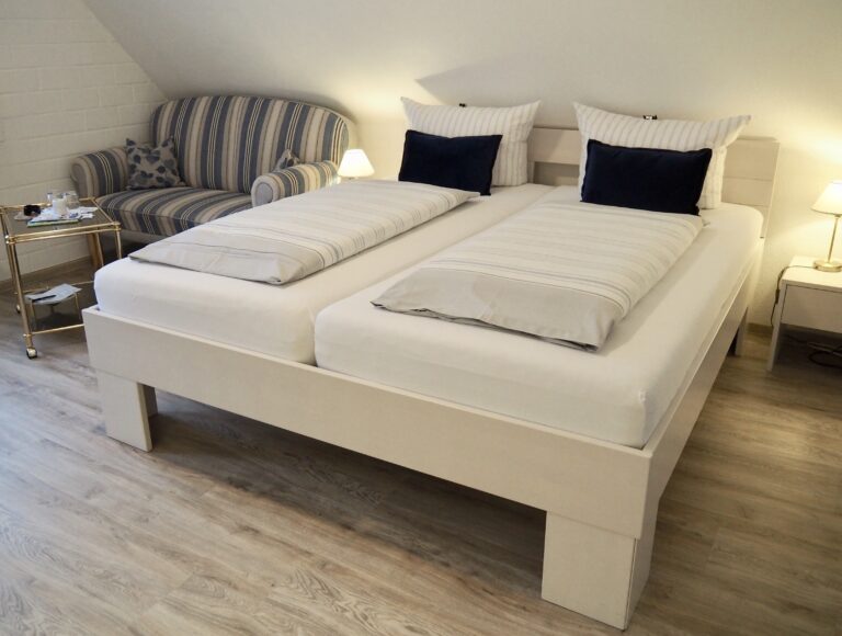Ansicht eines großen Doppelbett mit Nachtischlampen, im Hintergrund ein Sofa mit Beistelltisch